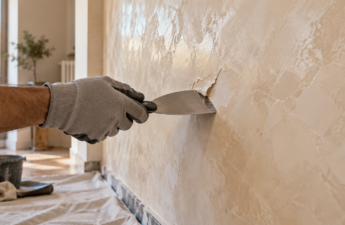 Mano con guanto che usa una spatola per rimuovere una piccola porzione di stucco veneziano da una parete beige